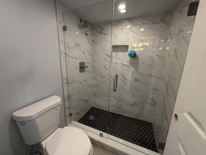 Walk in shower with marble look tile and frameless glass door