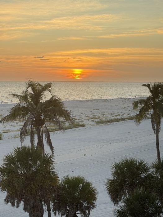 The sun dropping to the horizon over the Gulf, with the wide beach below the condo