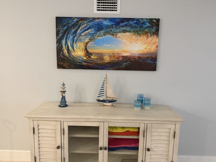 Living room console below a large wave canvas, with beach towels stocked for guests