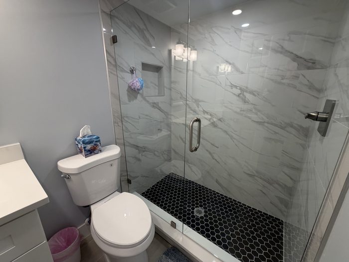 Guest bath walk in shower with marble look tile, black hex floor and frameless glass