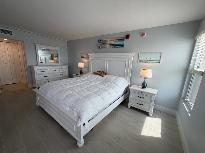 Primary bedroom with king bed, dresser and mirror, window to the beach
